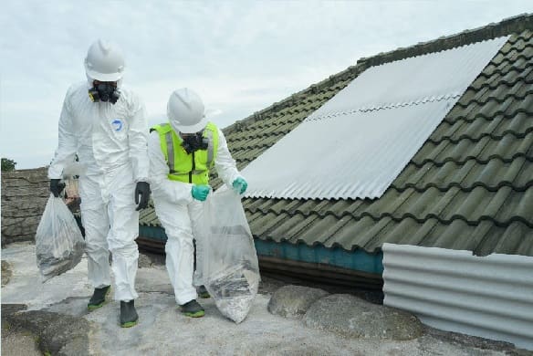 Asbestos removal workers carrying wrapped asbestos waste